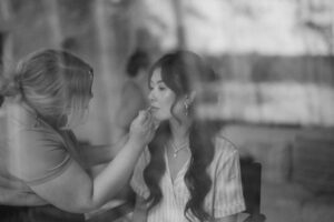 Woman applies makeup to seated bride.