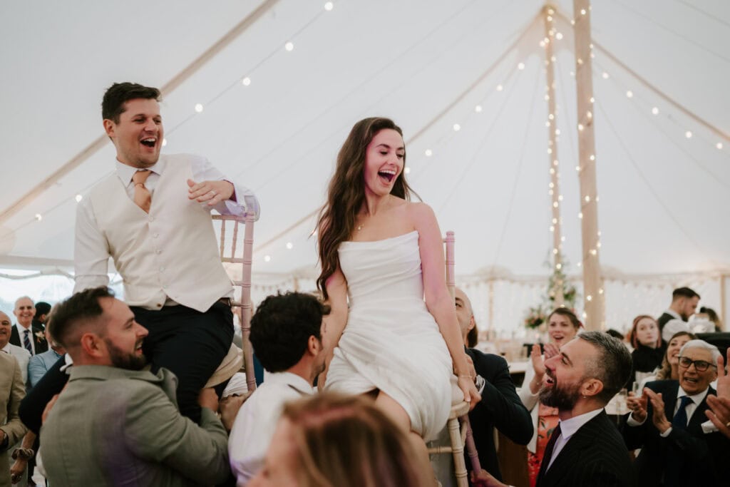 Bride and groom lifted on chairs at wedding celebration.