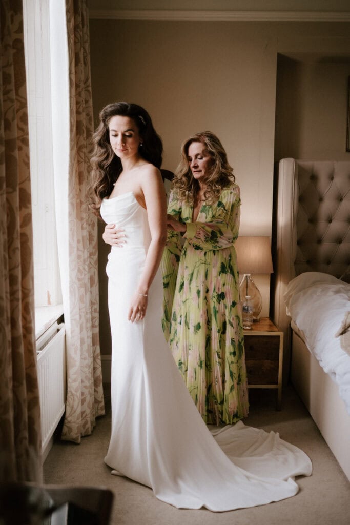 Woman helps bride dress in wedding gown.