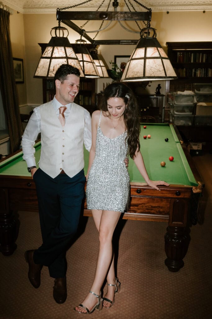 Couple smiling by pool table in dimly lit room.
