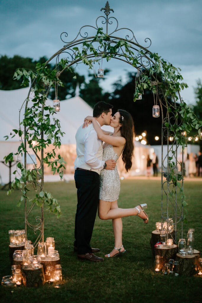 Couple kissing under decorative garden arch at night.