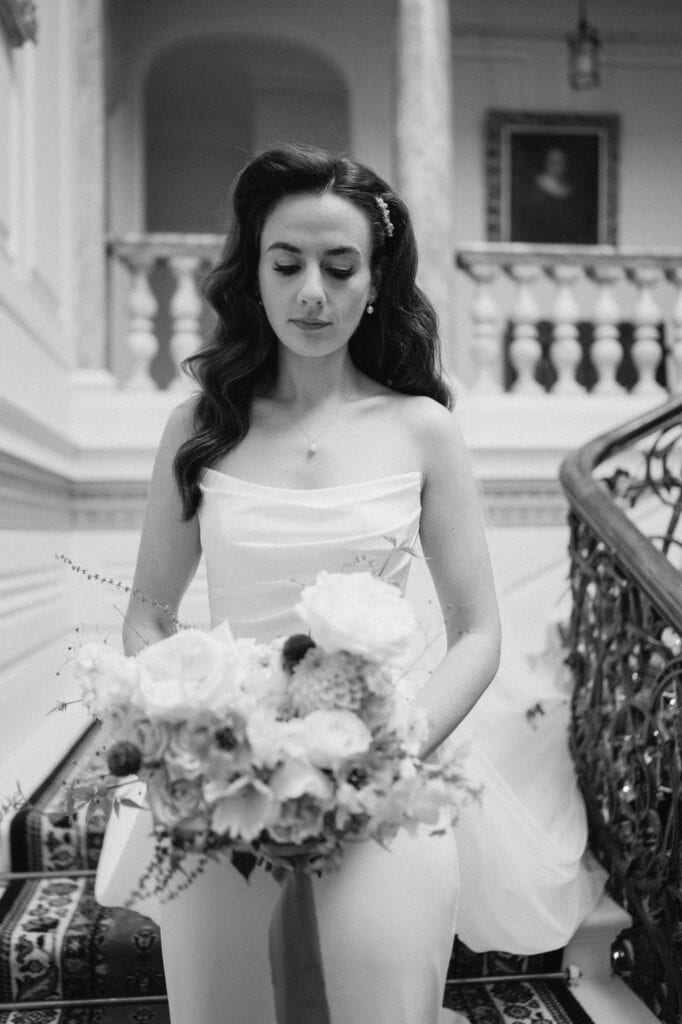 Bride holding bouquet on staircase, black and white photo.
