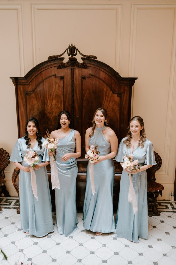 Bridesmaids in blue dresses holding bouquets, smiling.
