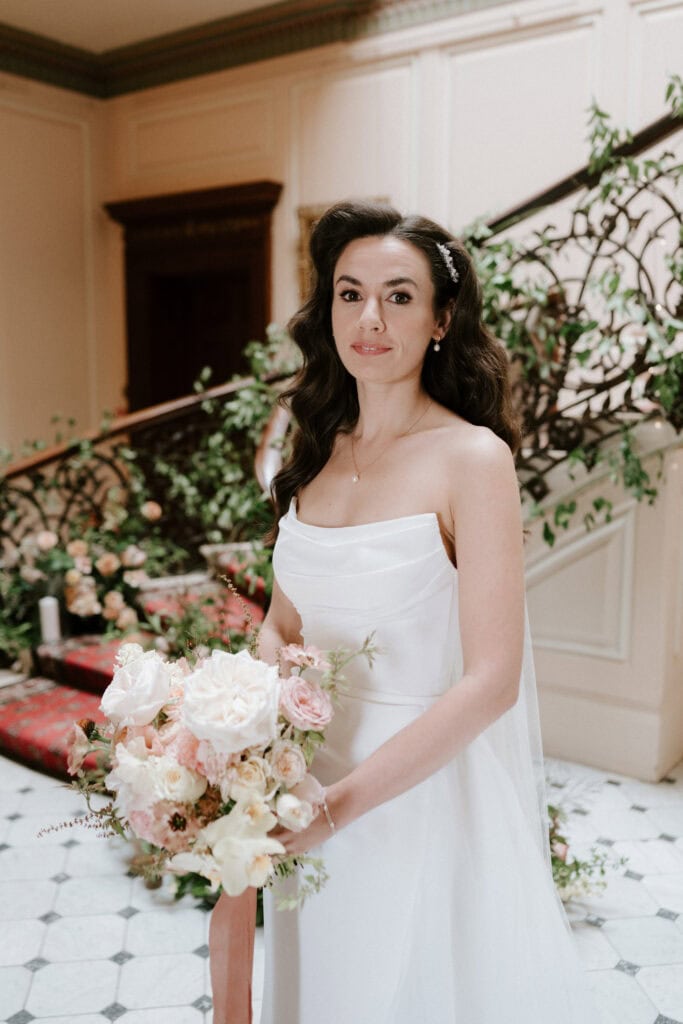 Bride holding bouquet on staircase indoors.