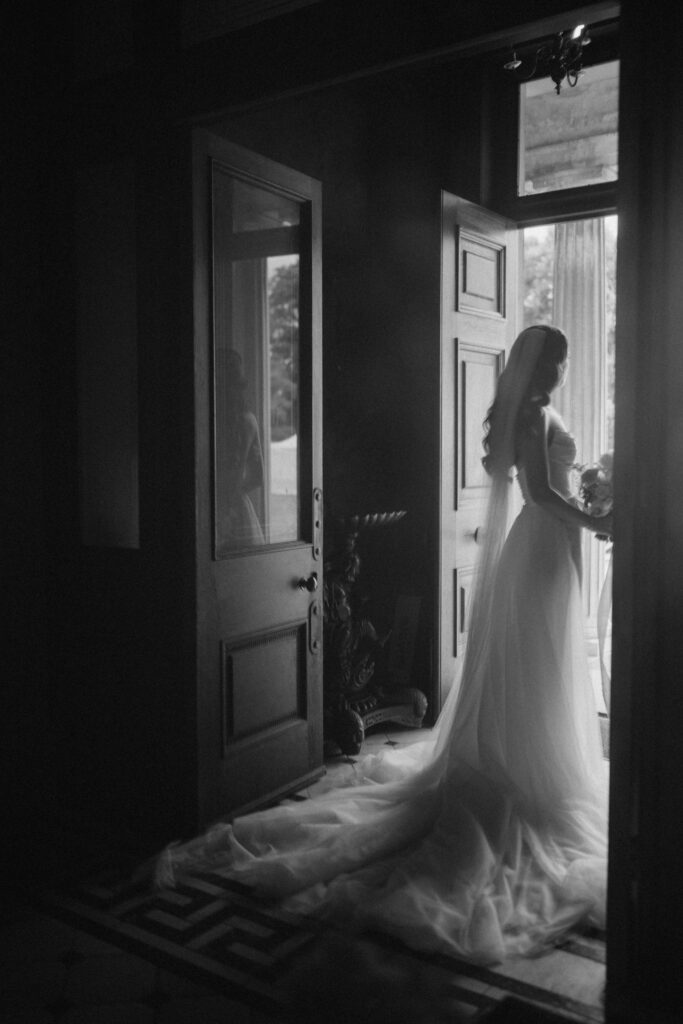 Bride in silhouette at open doorway with bouquet.