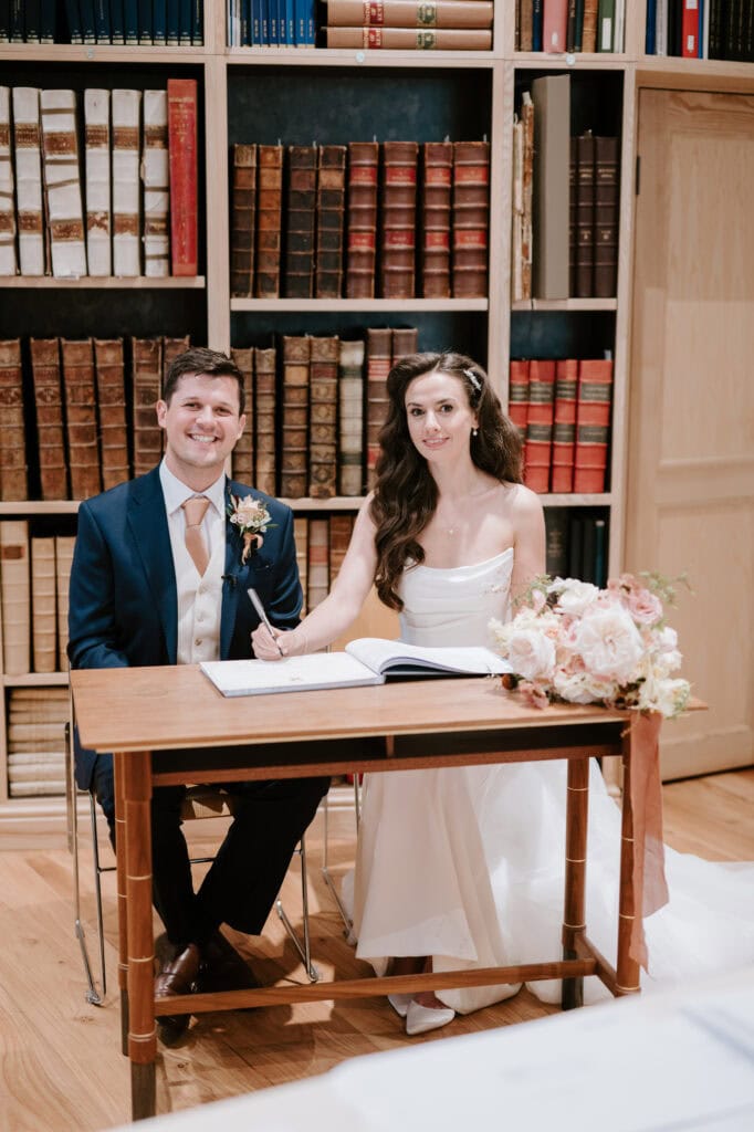 Couple signing marriage certificate in library setting.