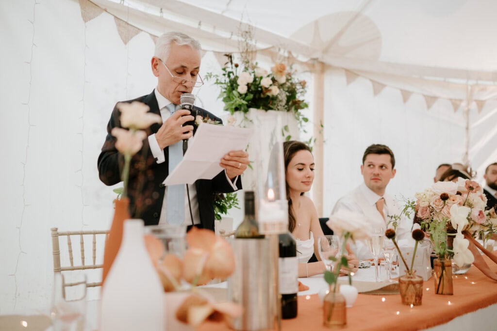 Man giving wedding speech at decorated table.