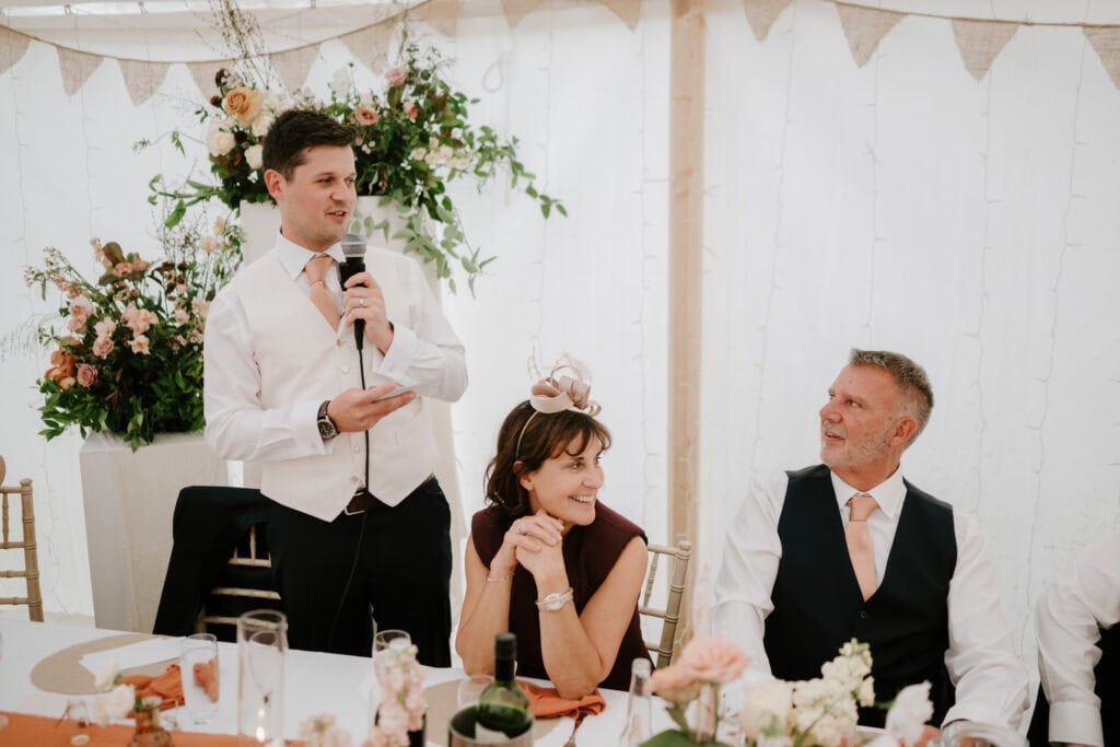 Man giving wedding speech at decorated table.