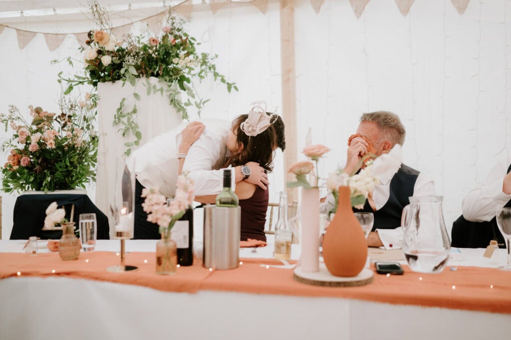 People hugging at a wedding reception table