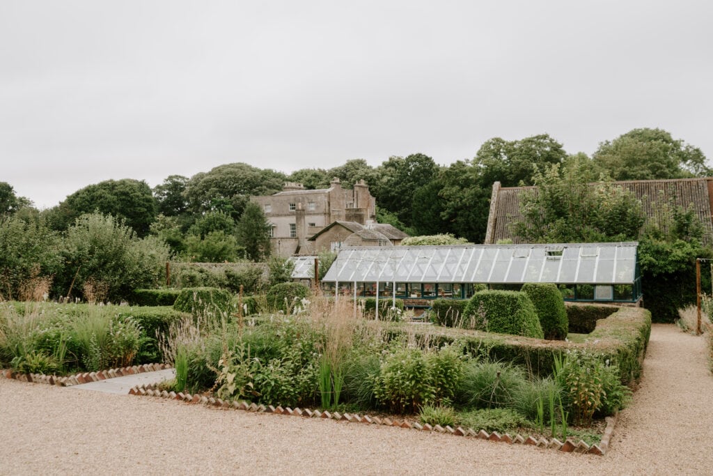 Lush garden with greenhouse and historic building.