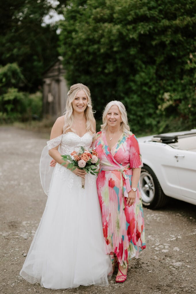 Bride and woman in colourful dress by white car