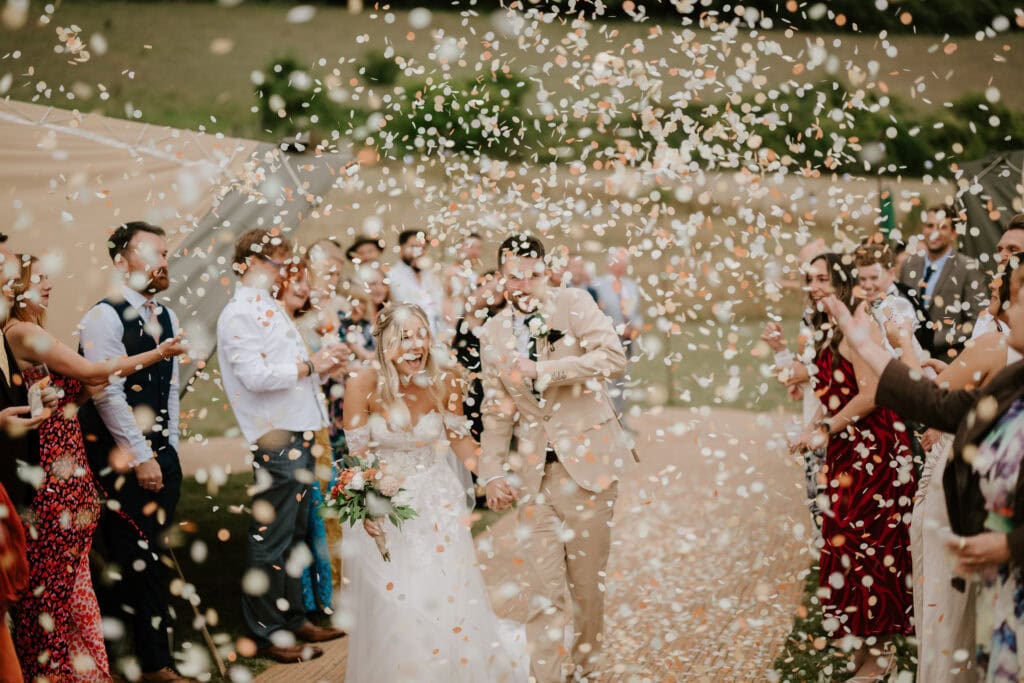 Cheerful wedding couple under shower of confetti.