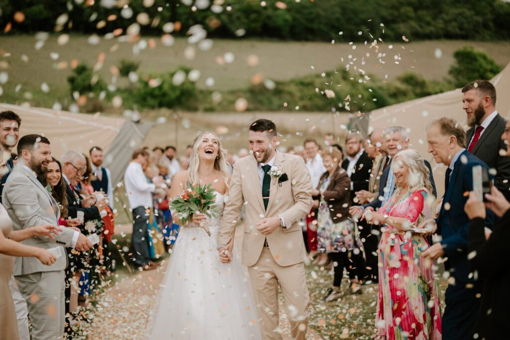 Newlyweds celebrate amidst outdoor wedding guests and confetti.