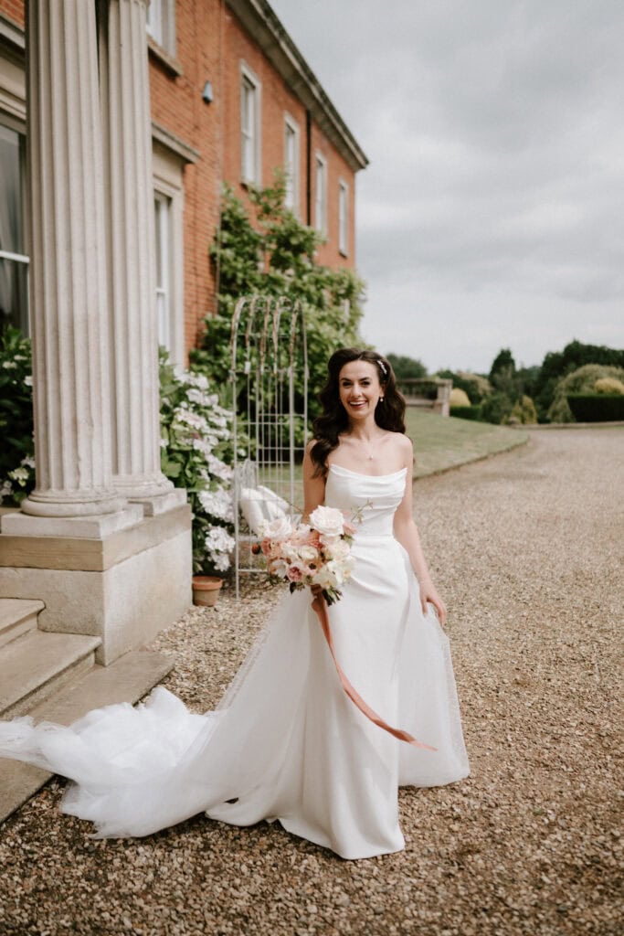 Bride in white gown holding bouquet outside mansion