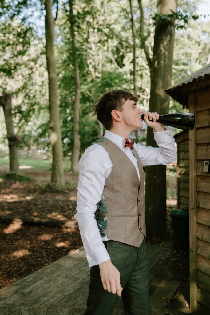 Man drinking from a bottle in forest wedding.