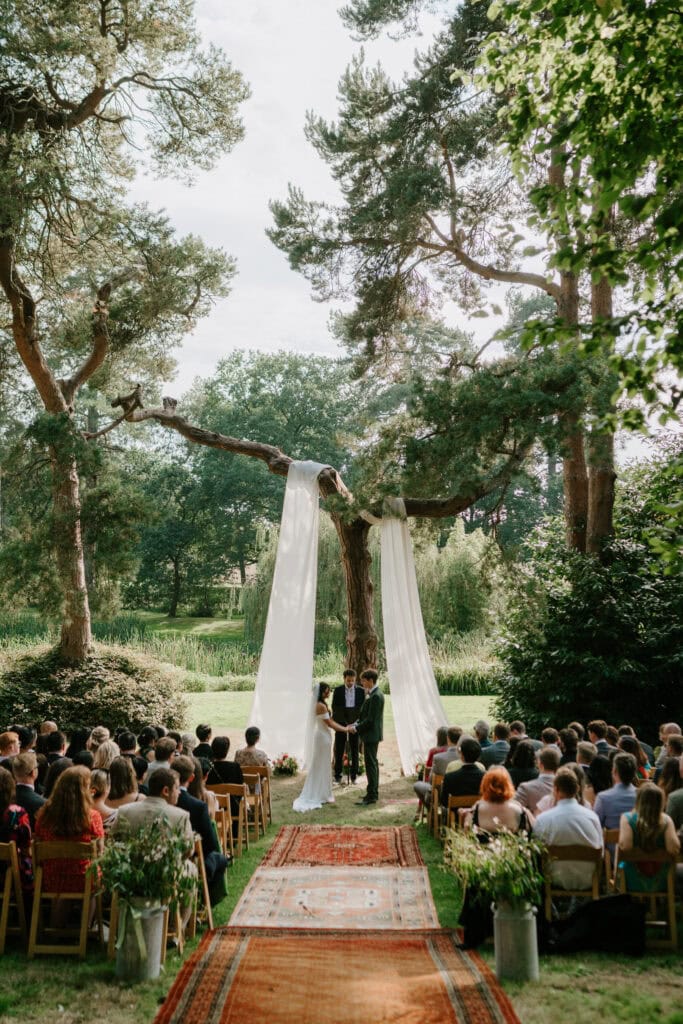 Outdoor wedding ceremony under trees and white drapes.