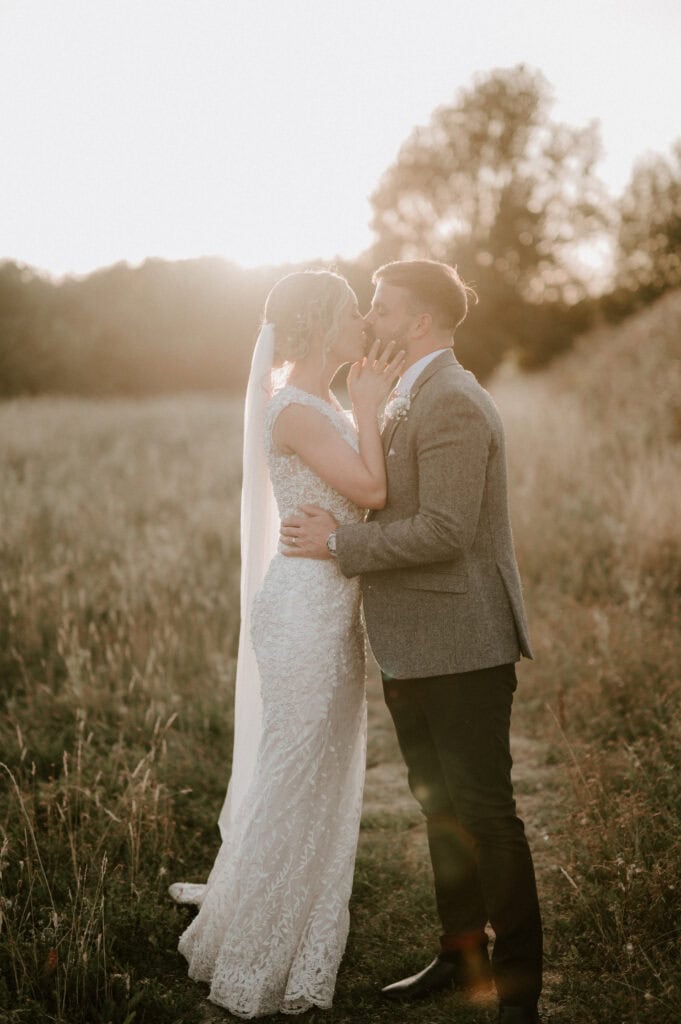 Bride and groom kissing in sunlit field.