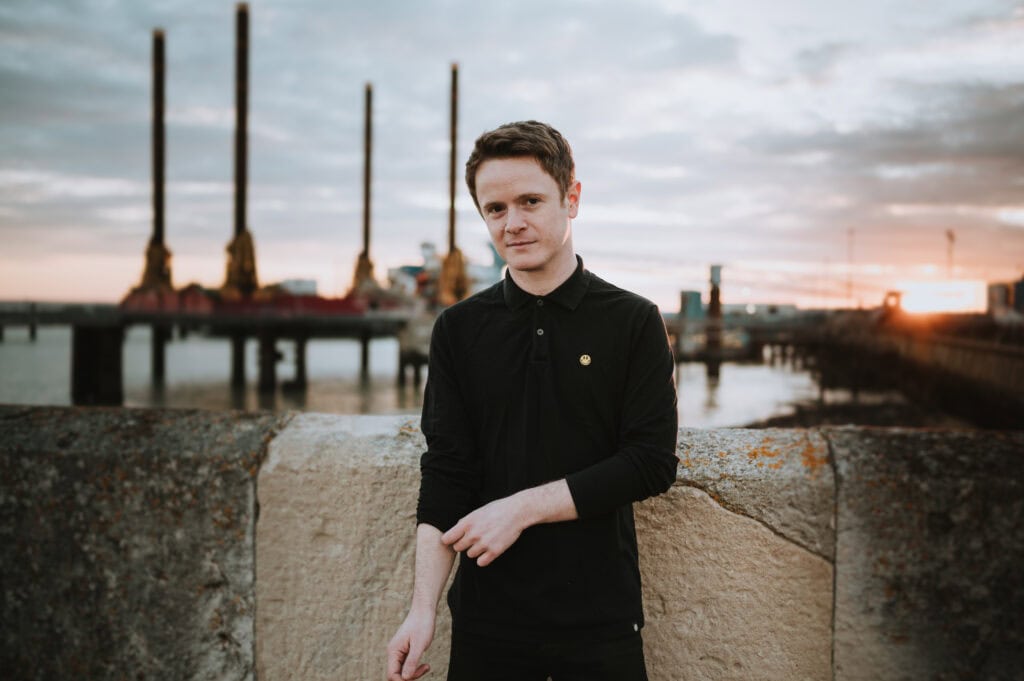 Person standing by industrial dock at sunset.