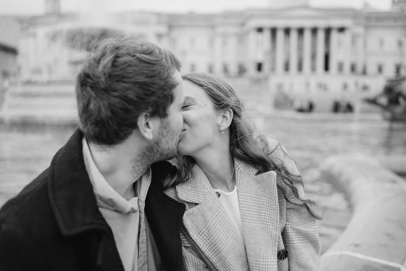 Couple kissing by a historic building fountain.