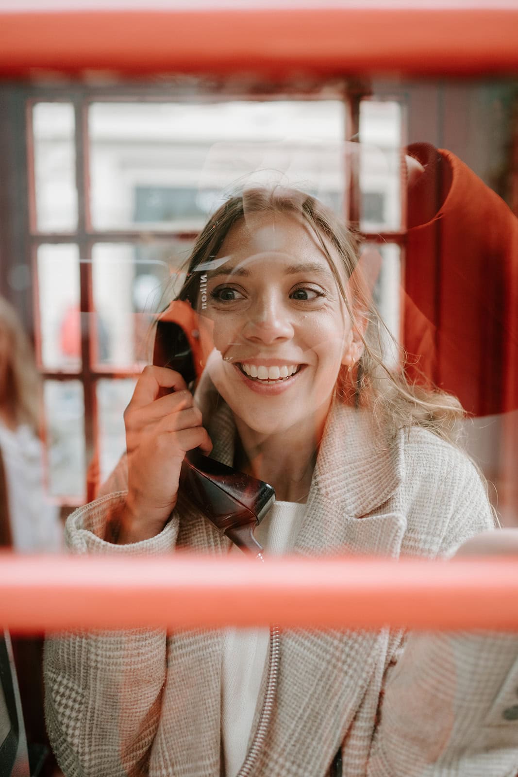 Woman smiling inside a red phone box.