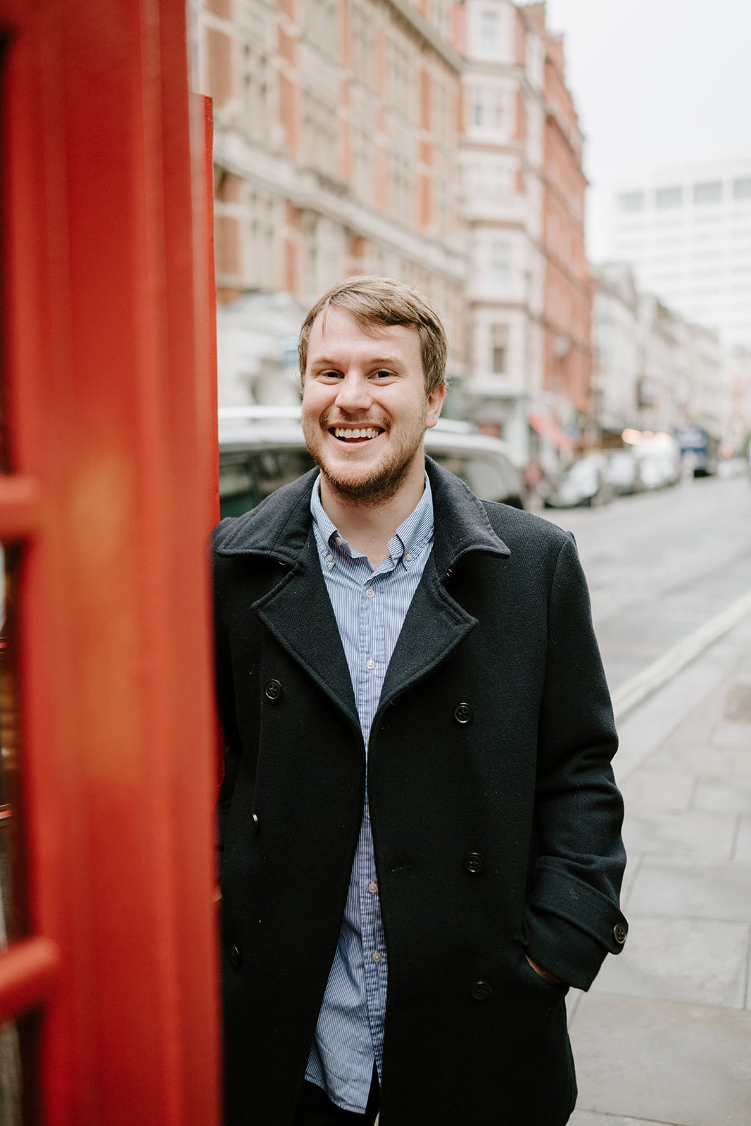 Smiling man near red phone box on street.