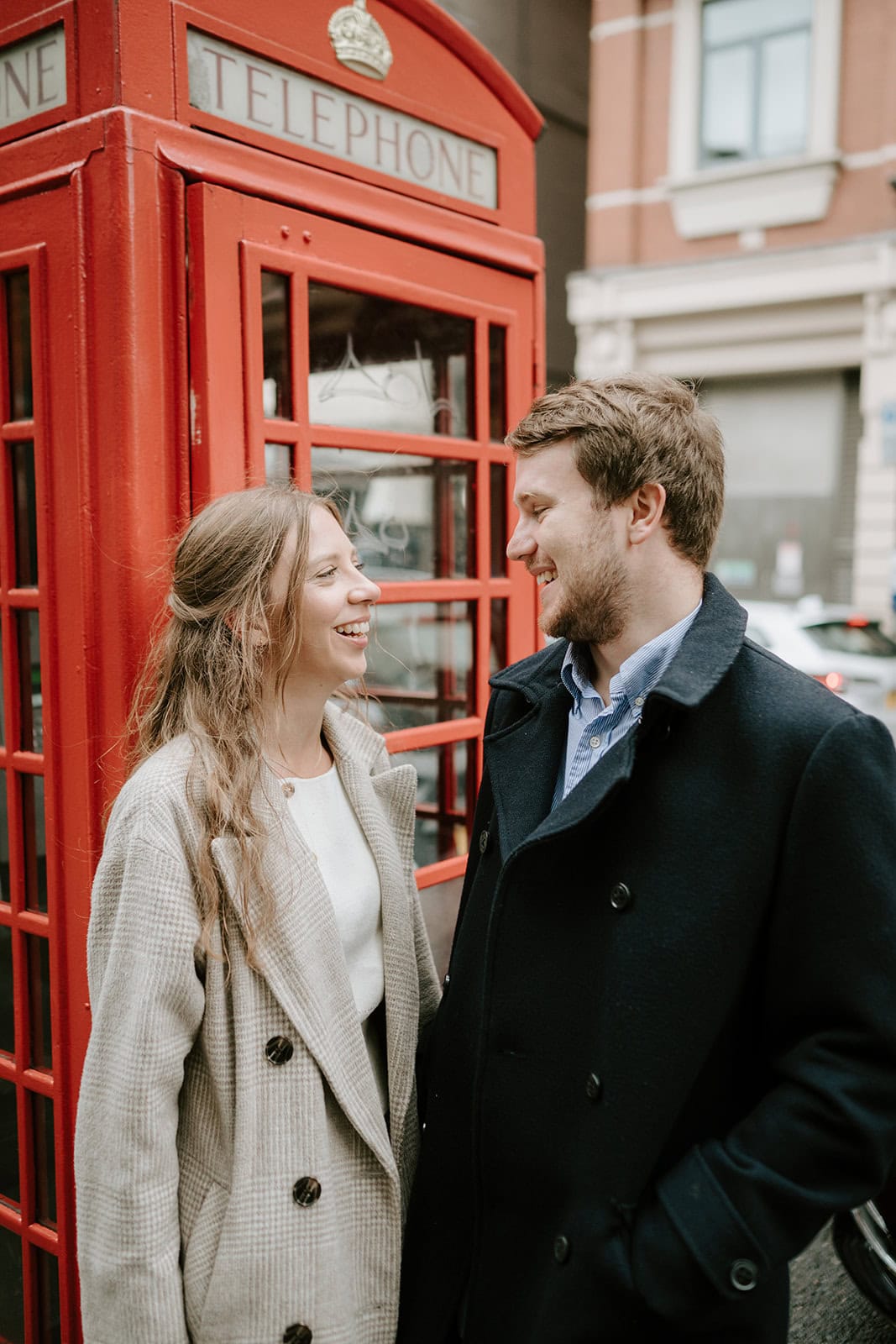 Couple smiling by a red telephone booth.