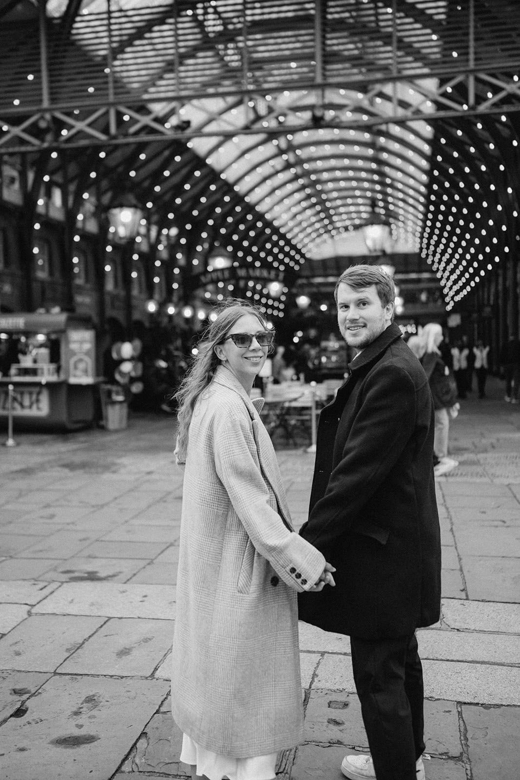 Couple holding hands in covered market, smiling.