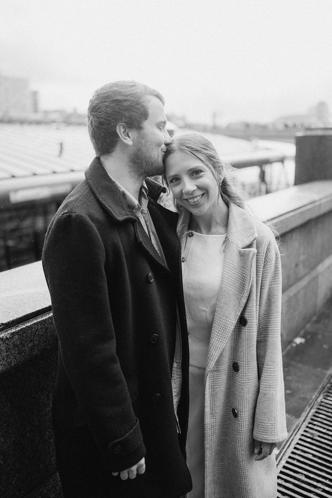 Smiling couple in coats on urban rooftop.