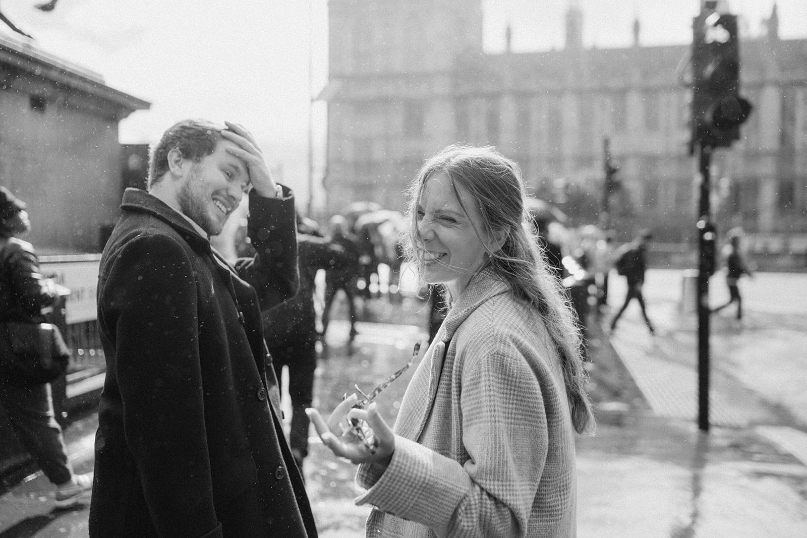 Couple laughing in rainy city street, black and white.