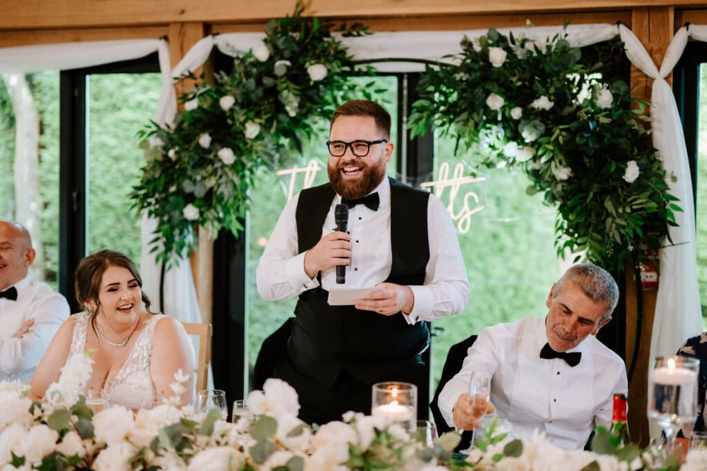 Groom giving wedding speech, guests laughing.