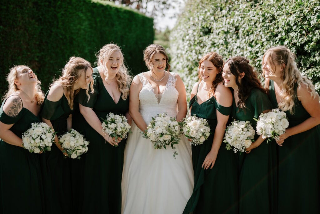 Bride with bridesmaids in green dresses, smiling outdoors.