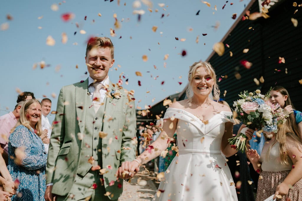 Happy couple walking through flower petals at wedding.