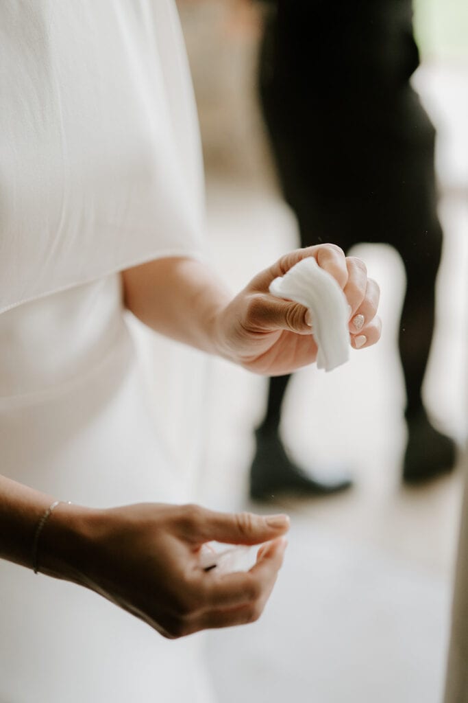A person in a white garment gently holds a small white cloth, evoking the serene elegance of a wedding. The background is softly blurred, with a faint silhouette of another person at Broadstairs. Image by Pearce Wedding Photography.