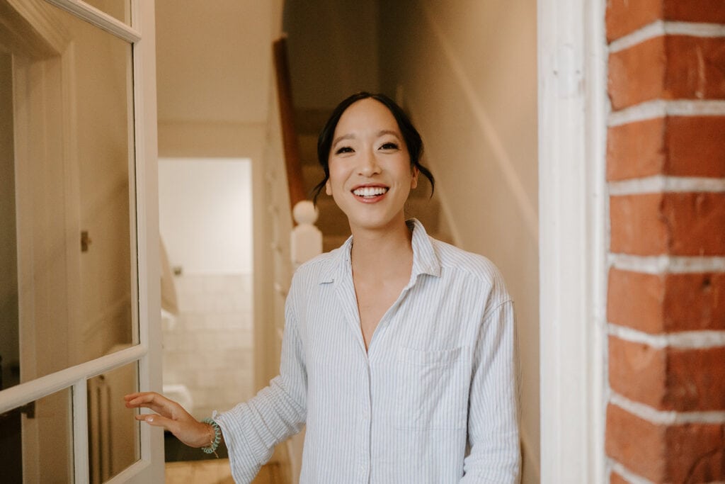 A person wearing a striped shirt smiles warmly while standing in an open doorway, reminiscent of a charming Broadstairs setting. With a glimpse of the staircase in the background, it feels like they're welcoming guests to a joyful wedding celebration. Image by Pearce Wedding Photography.