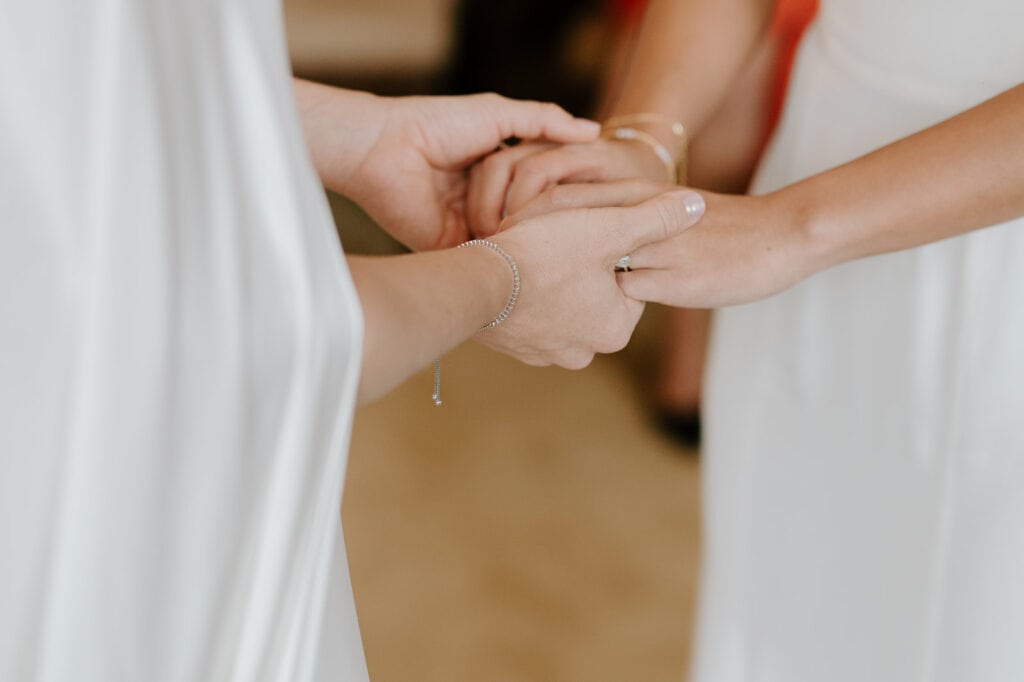 Two people in white attire hold hands tenderly, as if captured at a wedding, suggesting a moment of connection or support. The soft focus and neutral background enhance the intimacy of the scene, reminiscent of a serene moment by the seaside in Broadstairs. Image by Pearce Wedding Photography.