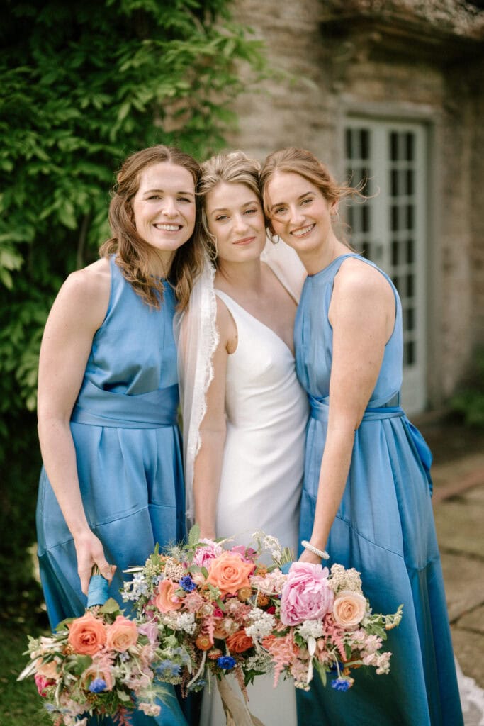 Bride with bridesmaids in blue dresses holding flowers.