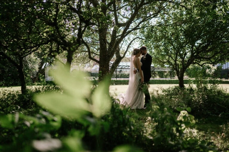 Bride and groom standing under trees in garden