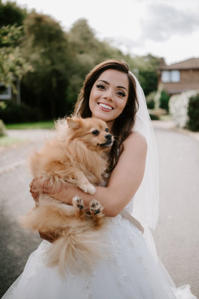 Bride smiling, holding fluffy dog, outdoor setting