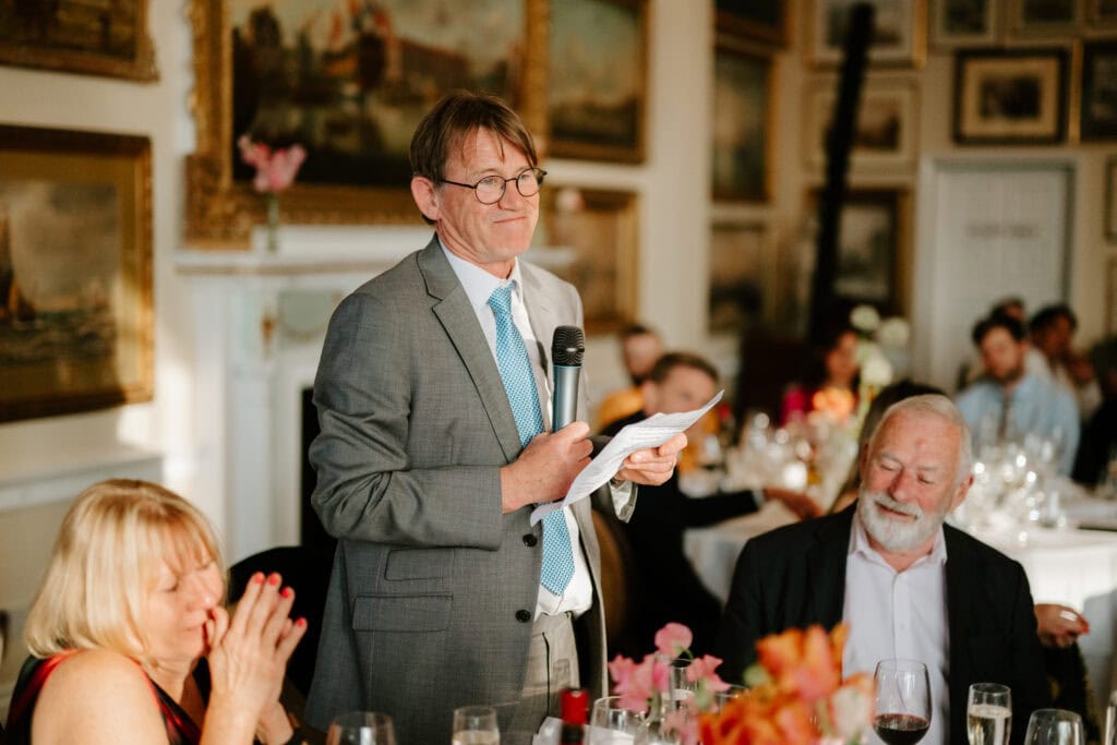 Man giving speech at formal event, holding microphone.