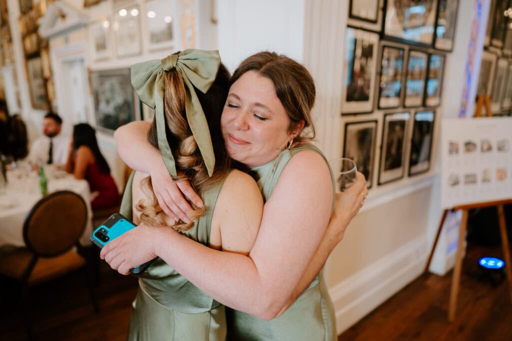 Two women in green dresses hugging at event.