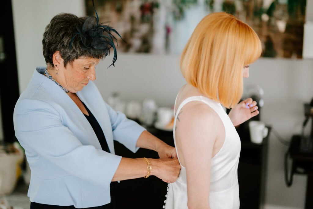 Woman helps fasten dress on another woman.
