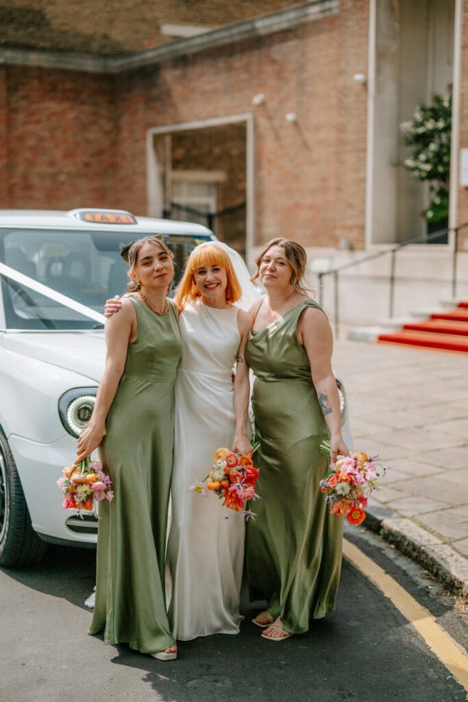 Bride and bridesmaids with flowers by a taxi.