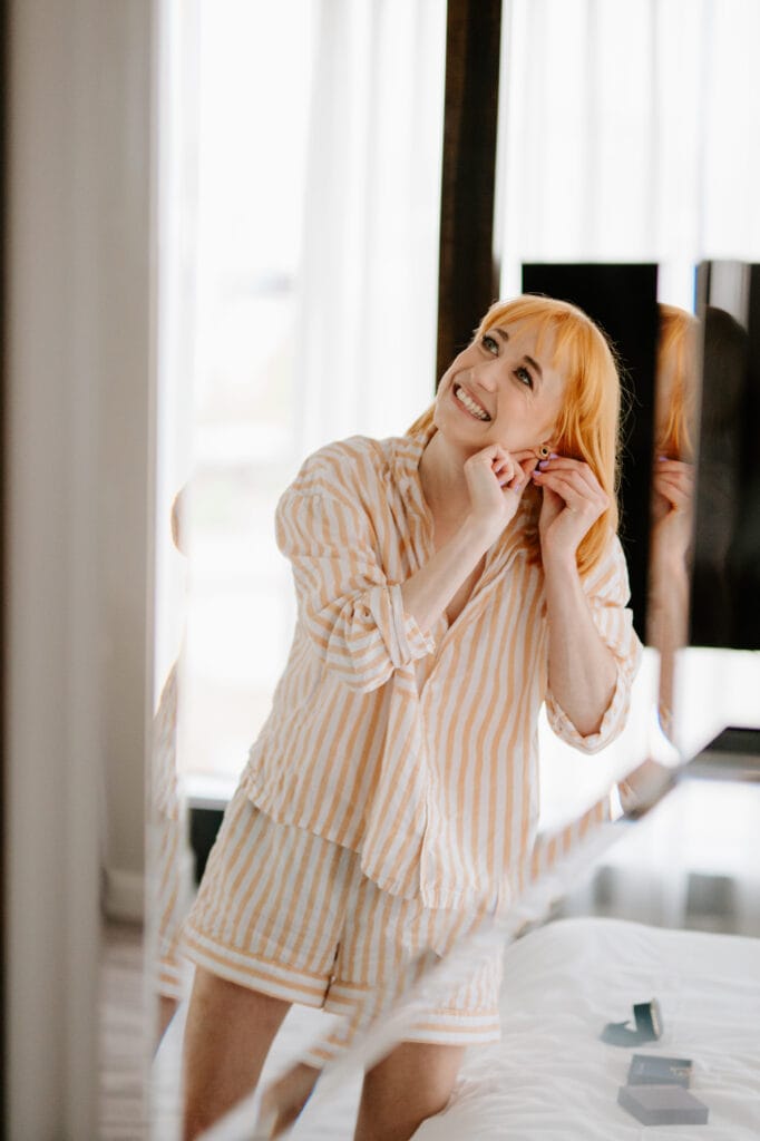Woman smiling while adjusting earrings in mirror.