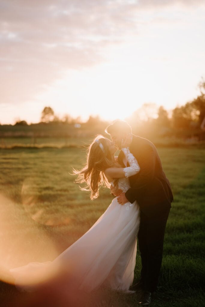 Couple kissing at sunset in field at cooling castle barn on their wedding day