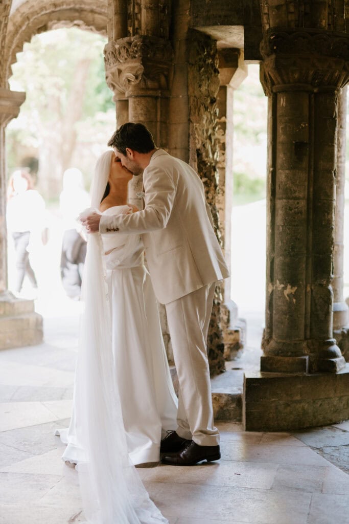 Bride and groom kissing in ancient stone archway.