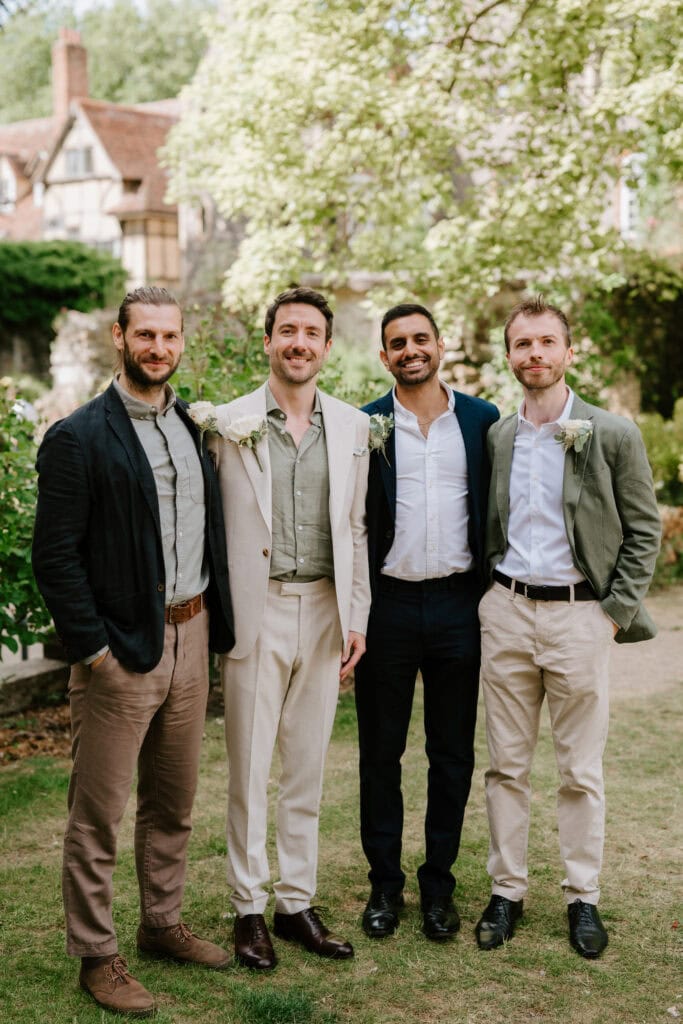 Four men posing outdoors, wearing suits, smiling happily.