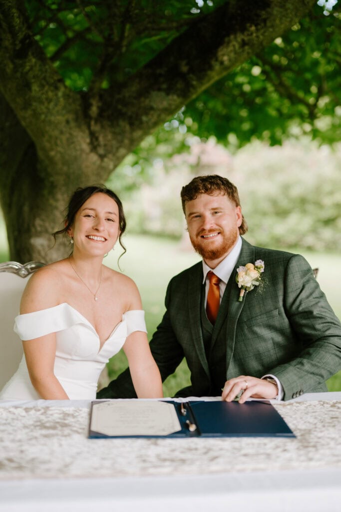 Couple smiling at marriage ceremony under tree.