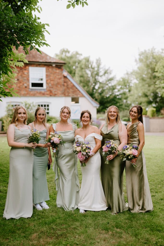 Bridesmaids in green dresses holding bouquets outdoors.