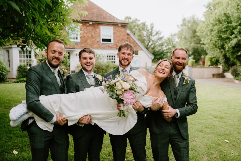 Groomsmen holding joyful bride in garden setting.