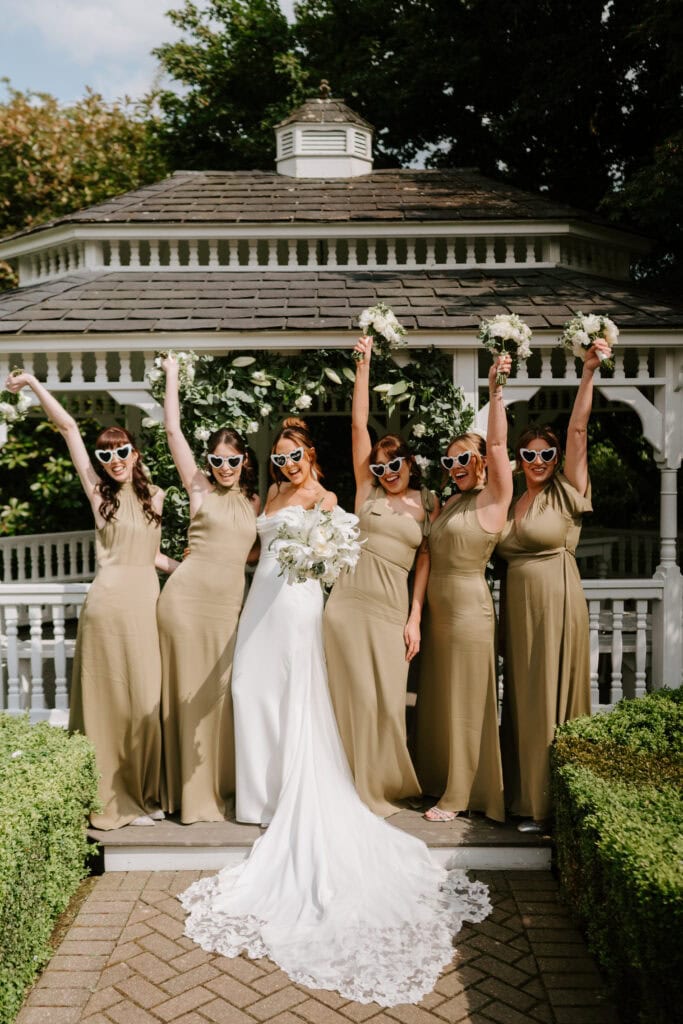 Bridesmaids and bride celebrate at outdoor wedding gazebo.